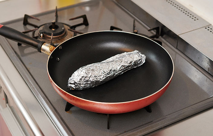 フライパンでアルミホイルに包んださつまいもを焼く