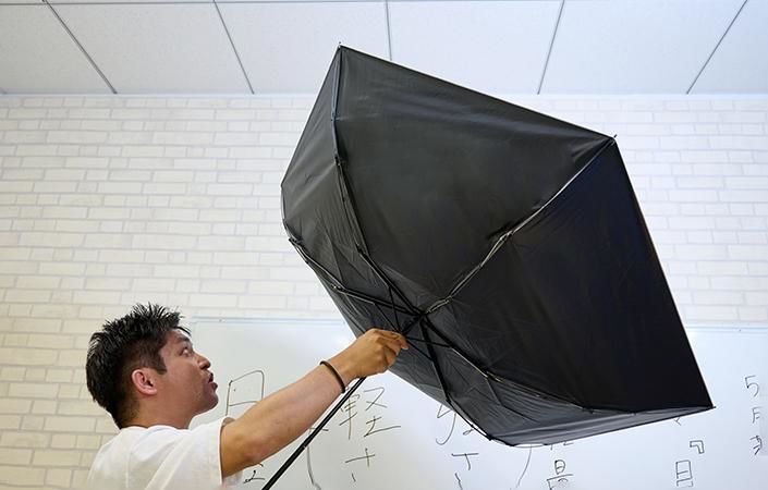 おちょこになった傘を持つ佐藤バイヤー